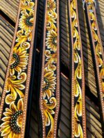 Close-up view of intricately tooled leather belts adorned with vibrant yellow sunflower designs. The belts, alongside a beautifully crafted Leather Dog Collar- Yellow Painted Sunflower- Tooled with similar sunflower motifs, are arranged on a wooden surface, showcasing detailed craftsmanship and rich, contrasting colors.