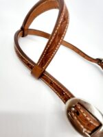 A close-up image of a Cowpuncher Sliding One Ear Headstall With Tooling with decorative stitching and intricate carvings along the straps. The bridle features a metal buckle and is set against a plain white background.