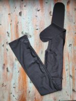 A pair of black Tail Bags laid out flat on a rustic wooden surface, reminiscent of the timeless quality found in Mane Bags. The tights are extended to show the legs and waistband clearly, with subtle light and shadow effects highlighting the fabric texture. The wooden surface has a distressed, weathered look with visible grain and knots.