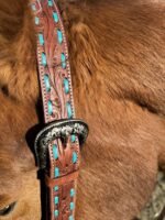 Close-up of a brown animal, possibly a horse or dog, wearing a Turquoise Buckstitch- Belt Style Split Ear Headstall. The leather collar is adorned with blue accents and features an ornate silver buckle with intricate designs. The animal's fur appears soft and well-groomed.