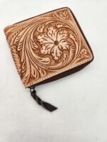 A small, square, light brown leather wallet with an intricate floral and leaf pattern carved into the surface. The wallet has a zipper closure with a dark brown leather pull tab. The background is a plain white surface.