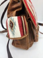 Close-up of a brown leather backpack featuring a side pocket with a colorful fabric design. The fabric has a red, white, light blue, and brown pattern, adding a stylish contrast to the leather. The image focuses on the side of the backpack.