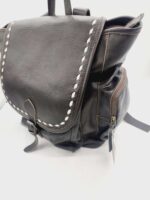 A dark brown leather backpack with white stitching along the flap edges is shown. The flap fastens with a buckle, and the bag has a zippered pocket on the side. The backpack is set against a plain white background.