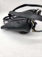 A black leather handbag with gold hardware and a shoulder strap is lying on a white surface. The bag is angled to show the side and bottom, highlighting the leather texture and strap attachments.