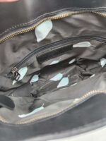 Open black handbag with a zippered pocket inside. The interior lining is black with a light blue and white leaf pattern.