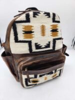 A backpack with a combination of brown leather and fabric featuring an intricate geometric pattern in black, white, and mustard. The design includes symmetrical shapes and lines, and the bag has multiple zippered compartments.