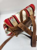 A brown leather backpack with patterned fabric accents on the top flap in red, white, and blue. The fabric features a geometric design. The backpack has adjustable leather straps and appears to be on a white surface.