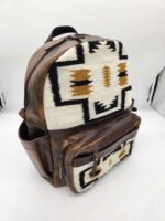 A brown leather backpack with Southwestern-style fabric panels featuring geometric patterns in white, black, and tan. The design includes a main compartment and two front pockets. The backpack is displayed against a plain background.