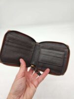 A hand holding an open brown leather wallet with a zipper around the edge. The wallet has multiple card slots on the left side and a smaller pocket on the right side. The background is plain white.