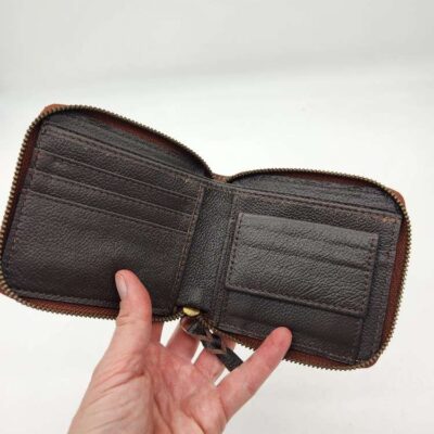 A hand holding an open brown leather wallet with a zipper around the edge. The wallet has multiple card slots on the left side and a smaller pocket on the right side. The background is plain white.