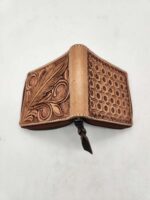 A handcrafted leather wallet with intricate design details is displayed on a white background. The wallet features floral and geometric patterns, with a zipper closure and a tassel pull. The leather appears to be aged for a rustic look.