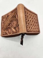 A handcrafted leather wallet with intricate patterns. One side features an elaborate leaf design, while the other showcases a geometric pattern of small circles and dots. The wallet is slightly open, revealing the texture and detail of the craftsmanship.