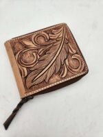 A brown leather wallet with an ornate, embossed leaf and swirl design on the front. The wallet has a zipper closure with a small, braided leather pull tab. The background is a plain, white surface.