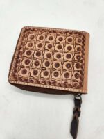 A small, square wallet made of brown leather with an intricate, geometric embossed pattern on the front. It has a zipper closure, and a braided leather zipper pull. The background is a plain white surface.