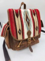 A brown leather backpack with a colorful woven textile flap featuring red, white, blue, and brown geometric patterns. The bag has a buckle closure on the front, two side pockets, and black shoulder straps. The background is plain and white.