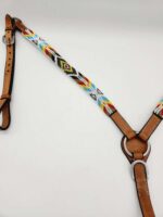 A close-up view of a horse breast collar featuring colorful beadwork on the straps. The bead design includes patterns in red, yellow, blue, black, and white. The leather parts are light brown and attached with metal rings and buckles.