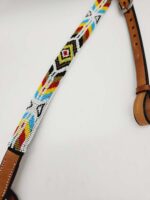 Close-up of a colorful beaded belt with geometric patterns. The belt features beads in colors such as red, yellow, blue, black, and white arranged in diamond and zigzag shapes. It has leather ends with adjustment holes and metal hardware.