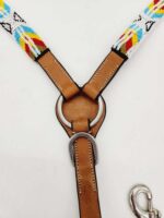 Close-up of a leather horse harness adorned with colorful, patterned beadwork. The harness features a ring in the center connecting three segments, with metal D-rings and a clip at the bottom. The beadwork includes vibrant blue, red, yellow, and white designs.