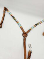 A leather horse breast collar with intricate, colorful beadwork featuring geometric patterns. The collar has metal rings and buckles for attachment, along with a metal snap hook for securing to other tack. The background is plain and white.