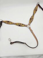 A decorative leather breastplate, featuring intricate yellow and brown floral patterns, a central silver buckle, and an attached tan strap with a metal clip. The breastplate is laid out on a white surface.