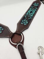 Close-up of a brown leather harness with teal floral embroidery and silver hardware. The harness features a circular metal ring at the center where the leather pieces connect and a silver clip attached to one end. The background is white.