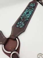 Close-up of a brown leather harness with decorative teal stitching. The harness features intricately designed floral patterns and metal rings, showcasing craftsmanship and detail. The background is plain white, emphasizing the harness's design.