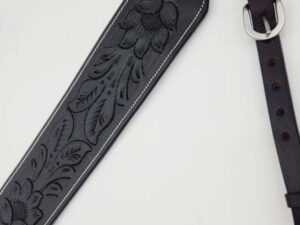 A close-up of a black leather guitar strap with intricate floral and feather embossing. The strap has a silver buckle and adjustable holes for fitting. The detailed craftsmanship highlights the texture and pattern on the leather.