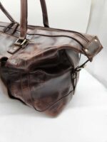 A close-up of a brown **Leather Duffel Bag- City Square** with a dedicated shoe pocket. The bag features a sturdy top handle, a zipper closure, and metal hardware. The leather appears to be slightly worn, giving the bag a vintage look. The background is plain white.