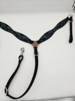 A black and blue dog harness is laid flat on a white background. The harness features a decorative copper-colored centerpiece and intricate blue floral patterns on the straps. It includes a leash attachment with a metal clip.