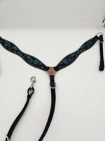 A black horse breast collar with intricate blue and green embroidery and a silver-tone center decoration is laid out flat on a white surface. It features silver rings and adjustable straps with clips.