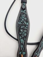 A close-up image of an intricately designed black leather strap. The strap features an embossed floral pattern with teal accents and detailed stitching along the edges. The leather appears to be of high quality with a glossy finish.