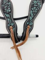 A close-up of intricately designed leather horse tack with blue and black floral patterns. The tack features brown leather straps and is positioned on top of a black and silver Sharpie marker, which is partially visible beneath the straps.