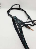 A black horse bridle with intricate turquoise stitching arranged on a white surface. The bridle features delicate, artistic patterns along its straps, showcasing detailed craftsmanship.