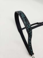 A black leather bridle with a teal and turquoise embroidered pattern rests against a white background. The bridle features intricate floral designs and silver hardware.