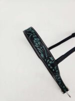 A close-up image of a black leather strap with an intricate turquoise floral design against a plain white background. The strap has metal buckles and appears to be part of an accessory, possibly a belt or a bag handle.