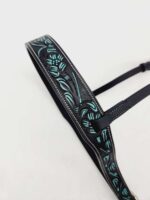 A black leather strap with intricate embossed floral designs in teal and green accents. The strap has stitching along the edges and a buckle for adjustment. The background is plain white.