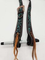 A piece of intricately designed leather gear, likely a part of horse tack, featuring a floral pattern in turquoise hues on a dark background. It has a decorative buckle and leather laces. A black marker is also visible in the image.