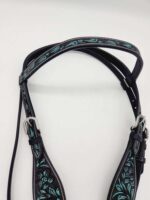 A close-up of a leather horse bridle with intricate turquoise embroidery on black leather. The bridle features silver buckles and hardware, and the detailed floral and paisley designs add a decorative touch. The background is a plain white surface.