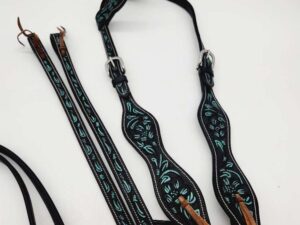 A black and teal western browband headstall is displayed against a white background. The headstall features intricate teal patterns and silver buckles, with leather ties at the ends. The reins, adorned with matching teal designs, are lying beside it.