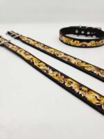 The image shows three leather pet accessories laid out on a white surface: two long leashes and a collar. They all feature a black base with a vibrant yellow floral pattern and metallic clasps or buckles.