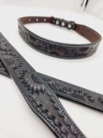 A close-up image of a black leather dog collar and leash set. Both pieces feature intricate embossed sunflower patterns. The collar has multiple adjustment holes and metal rivets, while the leash showcases matching decorative details.