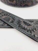 Close-up of black leather straps with embossed sunflower designs. The detailed texture shows two straps, one laying flat and another partially visible in the background. The background is a solid white surface.