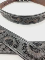 A close-up view of a leather belt and strap with intricate sunflower carvings. The leather is dark with a distressed finish, highlighting the detailed sunflower patterns. The background is white, emphasizing the craftsmanship of the leather work.