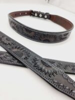 Close-up of a black leather belt with embossed sunflower designs. The belt features a polished buckle and several adjustment holes. The embossed sunflower patterns add an elegant and decorative touch to the leather accessory.