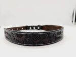 A close-up photograph of a dark leather belt with sunflower patterns embossed on it. The belt has silver-colored rivets and a buckle. The background is plain white, making the details of the belt stand out.