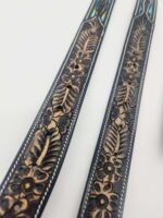 Close-up of two black leather straps with intricate embossed floral and leaf patterns. The designs feature detailed craftsmanship in natural shades, accented by stitch lines along the edges. The background is plain white.