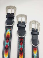 Three black leather belts with decorative metal buckles and colorful beaded designs in red, yellow, blue, and green. The buckles have intricate engravings, and each belt features a silver D-ring near the buckle. The belts are arranged on a white background.