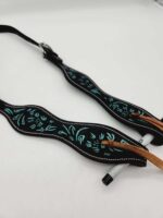 A close-up image of a black leather strap with blue floral embroidery and white stitching. The strap features a pen loop holding a white pen secured with a tan leather tie. The background is a plain white surface.