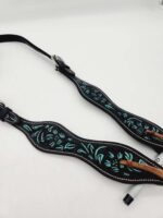 A black leather belt with intricate teal and brown embroidery lies on a white background. The belt features a wave-like pattern with floral designs and a silver buckle.