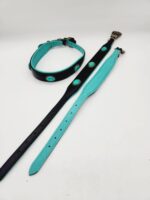 A set of two Leather Dog Collars- Natural Turquoise Stone and a leash placed on a clean white surface. The turquoise dog collars are primarily black with turquoise interior padding and turquoise circular embellishments. The leash is largely turquoise with a black exterior lining and metallic clasps.